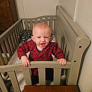 David joined the competition — help win amazing prizes! baby, child, crib, red_shirt, plaid, smiling, happy, indoor, wooden_crib, furniture, person, infant, hands, face, expression, home, room, cute, standing, young