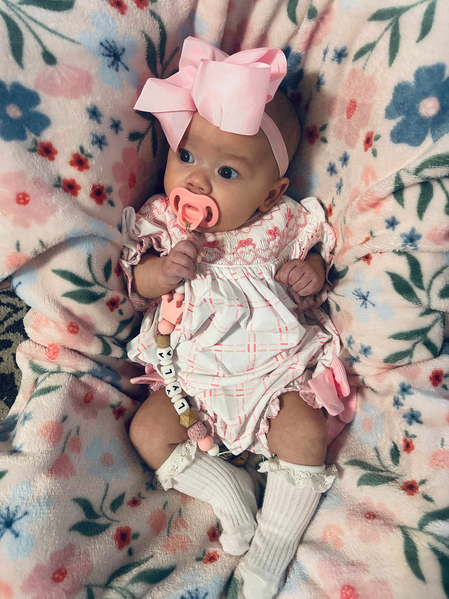 Lyla joined the competition — help win amazing prizes! baby, infant, pacifier, bow, blanket, floral_pattern, pink, white_socks, cute, clothing, portrait, child, indoors, soft_texture, cozy, lying_down, newborn, hand, face, wide_eyes