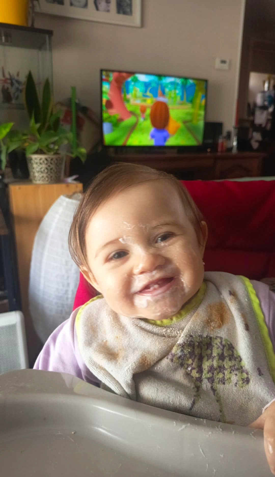 Jeanne participe au concours pour gagner de l'argent avec cette photo : baby, child, smiling, high_chair, bib, messy_face, food, indoor, living_room, television, cartoon, plant, furniture, person, portrait, cute, happy, home, casual, young_child