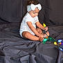 toddler, child, baby, headband, bow, lights, colorful_lights, sitting, curious, indoors, cloth_backdrop, wrinkled_cloth, playing, barefoot, white_onesie, portrait, young_child, toy, festive, cute