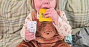 Caroline is registered to the contest to win money with this photo: toddler, child, baby, portrait, sitting, bed, bedroom, plaid, blanket, corduroy, overalls, brown_clothing, yellow_package, clothing_tag, holding, eating, blue_eyes, blond_hair, indoor, family_photo