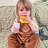 toddler, child, baby, portrait, sitting, bed, bedroom, plaid, blanket, corduroy, overalls, brown_clothing, yellow_package, clothing_tag, holding, eating, blue_eyes, blond_hair, indoor, family_photo