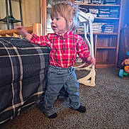 Caroline is registered to the contest to win money with this photo: child, toddler, standing, plaid_shirt, jeans, socks, indoors, living_room, bookshelf, books, couch, carpet, walker, toy, furniture, portrait, profile, blonde_hair, motion, home