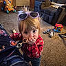 Caroline is registered to the contest to win money with this photo: child, toddler, portrait, sunglasses, red_plaid_shirt, blonde_hair, indoors, living_room, carpet, toys, toy_car, activity_cube, armchair, television, door, fashion, chewing, keyring, playtime, candid