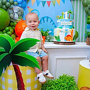 Sebastián is registered to the contest to win money with this photo: toddler, child, smile, birthday_cake, balloons, party, dinosaur, decorations, plant, table, shoes, shorts, shirt, smiling, indoor, celebration, colorful, props, happy, face
