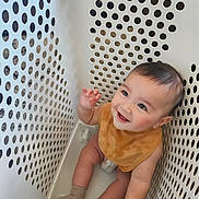 Odin is registered to the contest to win money with this photo: baby, child, smiling, laundry_basket, sitting, bib, socks, happy, cute, infant, playful, indoor, white, plastic, holes, closeup, portrait, cheerful, looking_up, young