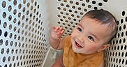 Odin is registered to the contest to win money with this photo: baby, bib, cheerful, child, closeup, cute, happy, holes, indoor, infant, laundry_basket, looking_up, plastic, playful, portrait, sitting, smiling, socks, white, young