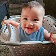 Odin joined the competition — help win amazing prizes! baby, smiling, laundry_basket, indoor, child, blue_bib, bracelet, playful, happy, face, hands, person, furniture, carpet, table, toy, cute, expression, infant, portrait