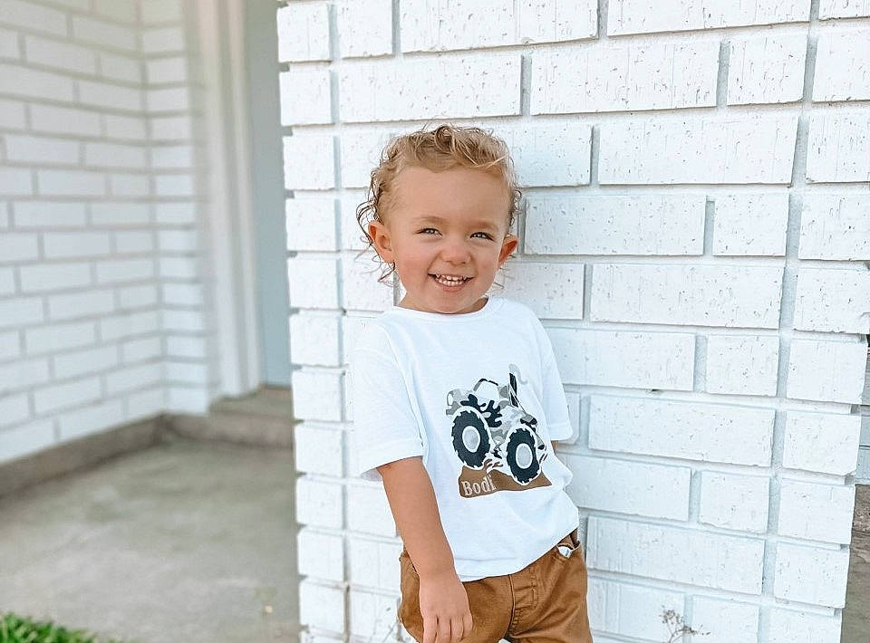 Bodhi is registered to the contest to win money with this photo: brick, brickwork, child, denim, door, flash_photography, grass, grey, happy, joy, pattern, person, plant, shorts, shoulder, sitting, sleeve, smile, street_fashion, t_shirt