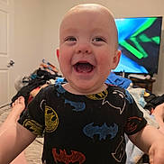 Alaric joined the competition — help win amazing prizes! baby, child, smiling, indoor, bedroom, tshirt, batman_logo, television, furniture, blanket, feet, person, happy, portrait, candid, skin, head, room, clothing, home