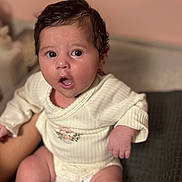 Selena a rejoint le concours — aidez-le/la à gagner de superbes lots ! baby, infant, child, surprised, face, skin, hair, clothing, onesie, hand, legs, person, indoors, soft_light, blurred_background, expression, cute, young, portrait, sitting