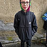 backpack, boy, casual_clothing, child, concrete_wall, glasses, hands_in_pockets, hoodie, jacket, outdoor, portrait, school_kid, short_hair, smile, sneakers, standing, street, urban, wet_drops, young_person