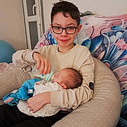 Mathieu a rejoint le concours — aidez-le/la à gagner de superbes lots ! child, baby, sibling, feeding, bottle, glasses, pillow, blanket, stuffed_animal, blue_toy, sofa, indoor, portrait, newborn, smile, nursery, casual_clothing, family, home, cuddle