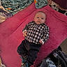 baby, bedroom, blanket, child, clothing, colorful, curious, fabric, face, footwear, indoor, infant, lying_down, pants, person, pink_blanket, shirt, sneakers, soft_texture, young_child