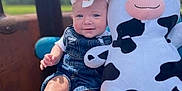 Bug is registered to the contest to win money with this photo: baby, blue_cushion, bow, child, cloudy_sky, cow, cute, denim, happy, infant, nature, outdoor, overalls, person, plush_toy, portrait, sitting, smile, sunny, toy