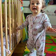 Julia participe au concours pour gagner de l'argent avec cette photo : baby, child, colorful, crib, curious, cute, expression, floor_mat, foam_mat, furniture, home, indoor, pajamas, person, playroom, portrait, standing, toddler, toy, wooden_crib