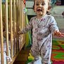 baby, child, colorful, crib, curious, cute, expression, floor_mat, foam_mat, furniture, home, indoor, pajamas, person, playroom, portrait, standing, toddler, toy, wooden_crib