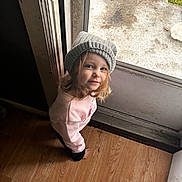 Freyja joined the competition — help win amazing prizes! barefoot, casual, child, curly_hair, door, floor, glass_door, gray_hat, hat, home, indoor, looking_up, natural_light, pink_clothing, portrait, smile, sweatshirt, toddler, wooden_floor, young_child