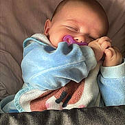Nélya participe au concours pour gagner de l'argent avec cette photo : baby, sleeping, pacifier, blanket, bed, blue_clothing, infant, peaceful, cute, child, resting, soft, indoors, cozy, hands, face, head, young, toddler, comfort
