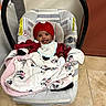 baby, bib, blanket, car_seat, child, clothing, cozy, cute, floor, happy, indoor, infant, knit_hat, minnie_mouse, person, red_hat, seat, smile, striped, tile_floor