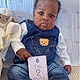 baby, blue_background, card, child, clothing, couch, cute, denim_overalls, expression, face, feet, hands, indoor, infant, lamb, plush_toy, portrait, seated, sneakers, white_shirt