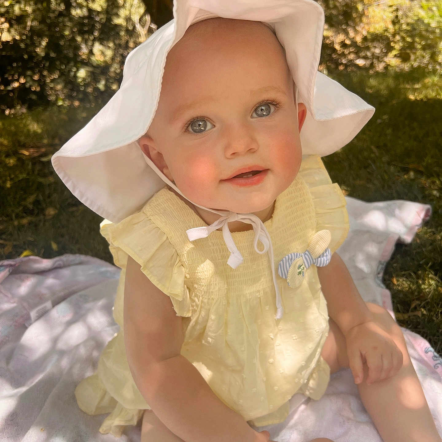 Calah is registered to the contest to win money with this photo: baby, blanket, child, cute, face, grass, happy, nature, outdoor, person, playful, portrait, sitting, skin, smiling, summer, sunhat, sunlight, yellow_dress, young