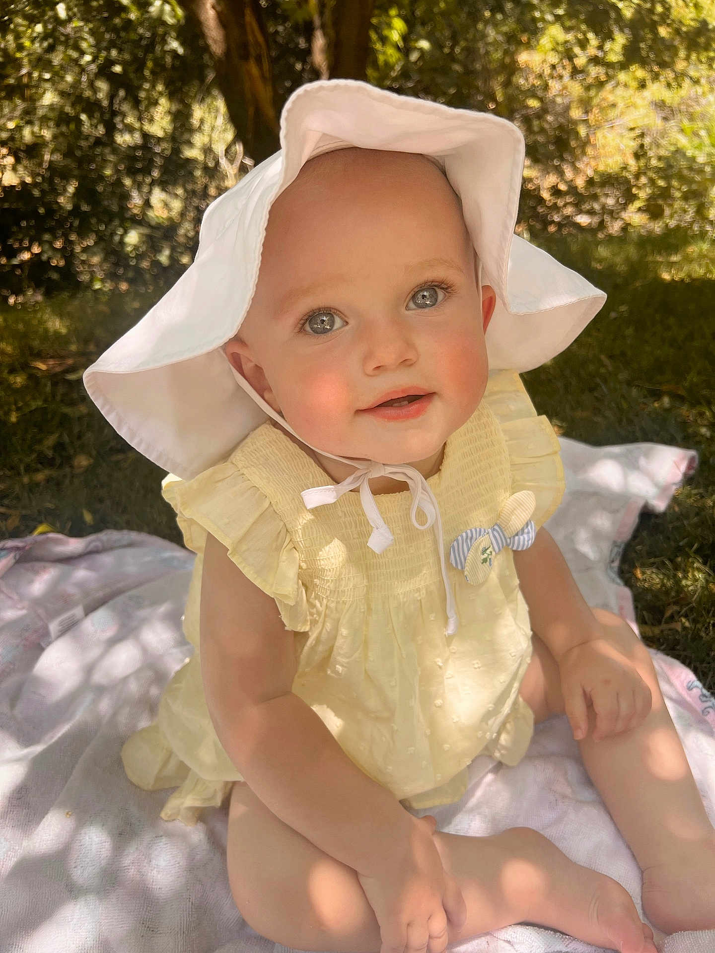 Calah is registered to the contest to win money with this photo: baby, child, outdoor, sunhat, yellow_dress, blanket, grass, smiling, face, skin, sunlight, nature, person, sitting, cute, summer, young, happy, playful, portrait
