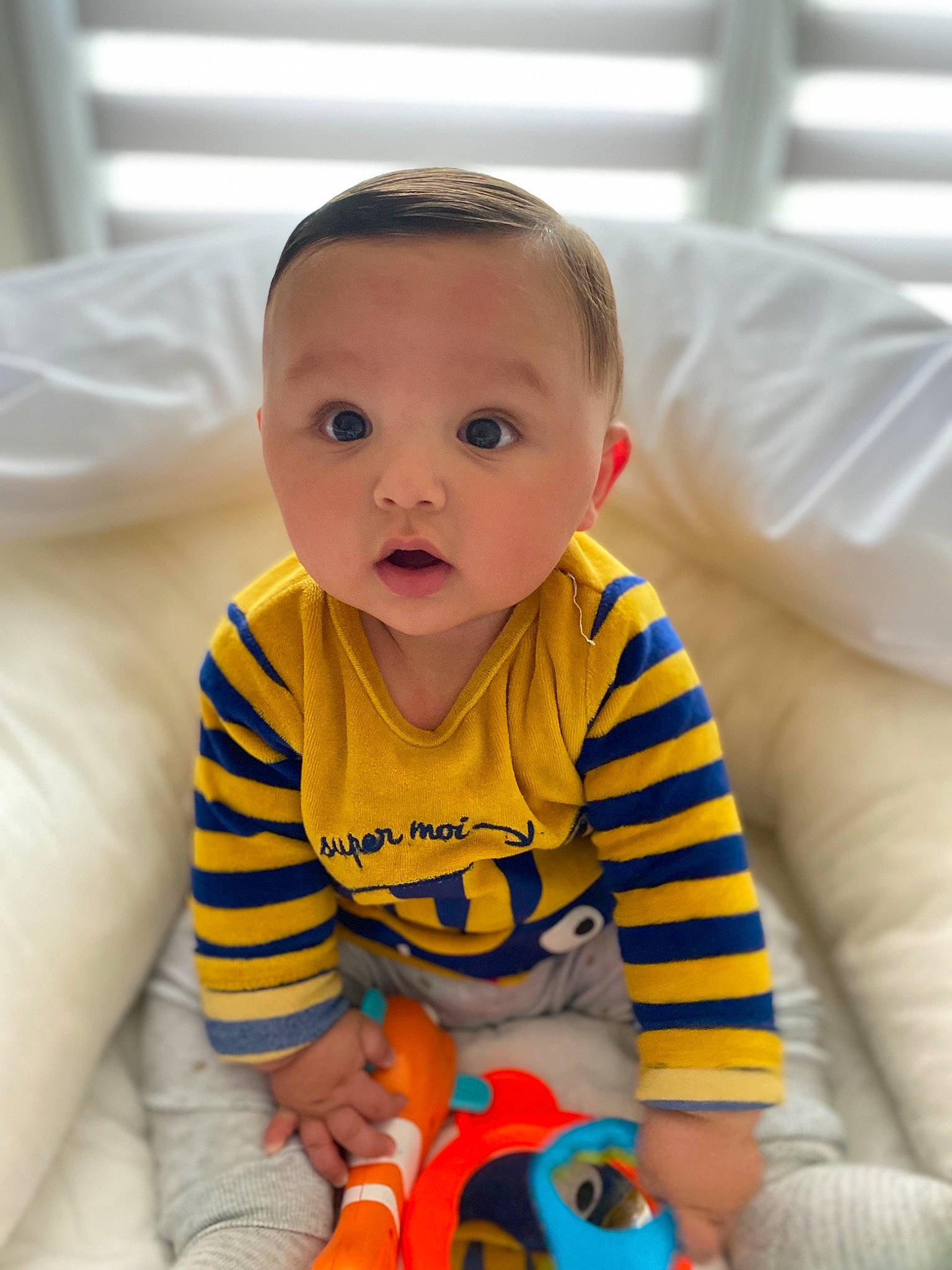 Ismaël participe au concours pour gagner de l'argent avec cette photo : baby, baby_playing_with_toys, baby_products, baby_toddler_clothing, cheek, comfort, eye, finger, flooring, happy, head, nose, orange, person, room, sitting, skin, sleeve, surprise, t_shirt