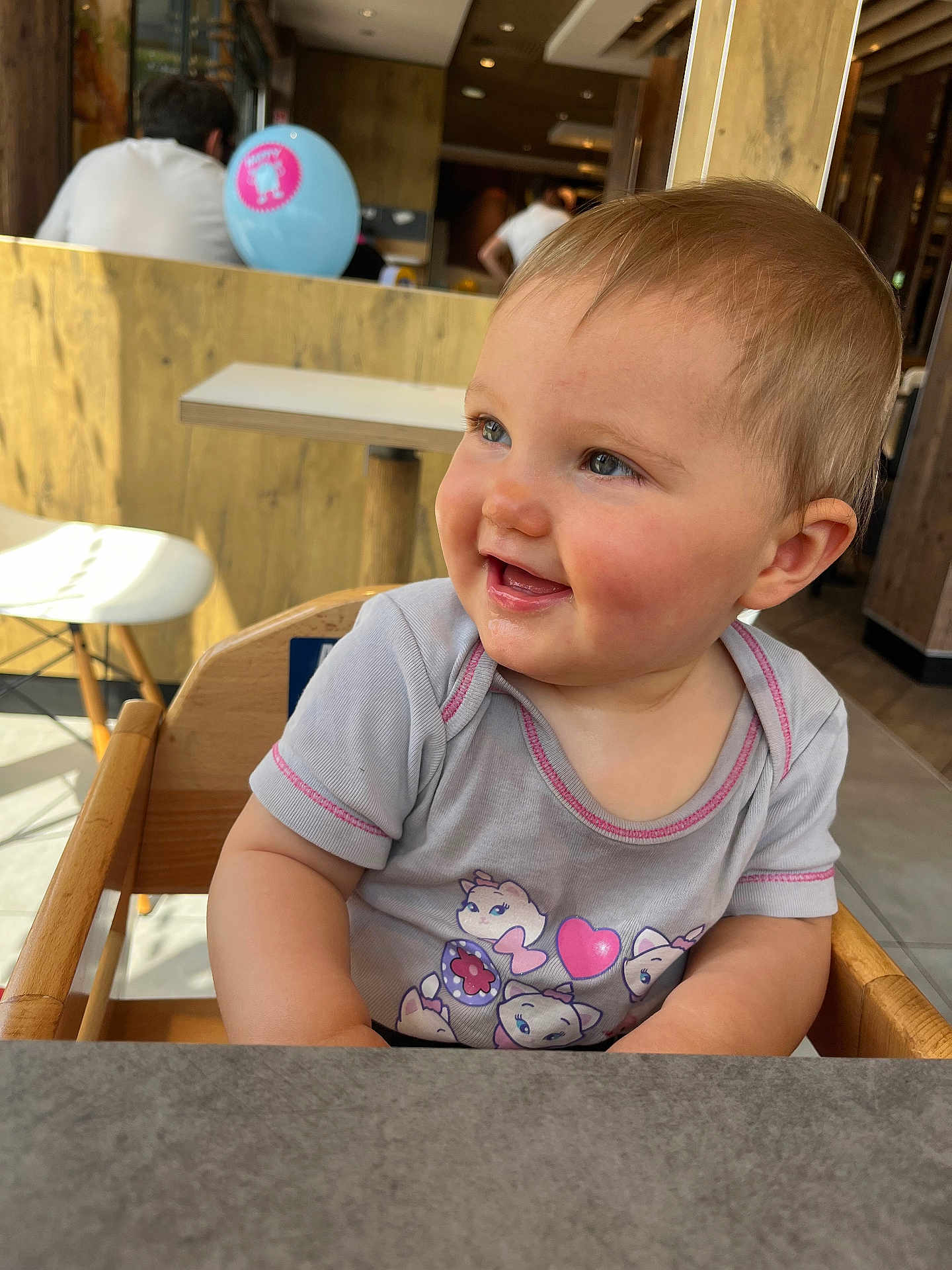 Hanaé participe au concours pour gagner de l'argent avec cette photo : baby, child, smile, high_chair, indoor, shirt, cartoon, balloon, wooden, table, person, happy, face, cute, toddler, blue_eyes, short_hair, casual_clothing, daylight, restaurant