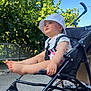 baby, stroller, hat, outdoor, child, legs, feet, sunlight, greenery, blue_sky, sitting, cute, summer, infant, casual_clothing, daytime, nature, person, expression, relaxing