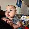Xavier is registered to the contest to win money with this photo: baby, child, infant, portrait, indoor, living_room, couch, blanket, plush_toy, gray_shirt, wide_eyes, surprised, curious, sitting, hands, face, head, soft_lighting, home, family_photo