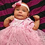 adorable, baby, blanket, bow, child, clothing, cute, expression, fabric, fist, headband, indoors, infant, laying_down, newborn, person, pink_dress, portrait, small, striped_blanket