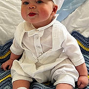 Christopher is registered to the contest to win money with this photo: baby, child, white_clothing, hat, sitting, blanket, knitted_blanket, indoors, cute, portrait, smiling, footwear, socks, face, blue_eyes, infant, hands, cheeks, cute_expression, soft_lighting