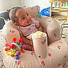 baby, infant, inflatable_seat, toy, colorful_toy, indoor, child, happy, smiling, seated, patterned_floor, wooden_shelf, plant_pot, purple_clothing, face, cute, small, home, decor, playful