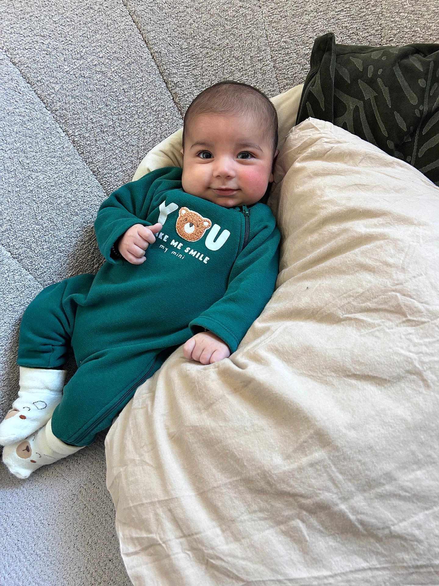 Sayël a rejoint le concours — aidez-le/la à gagner de superbes lots ! baby, infant, child, onesie, green_onesie, pillow, cushion, sofa, couch, smile, face, cheeks, eyes, socks, blanket, textile, home_interior, portrait, relaxed, soft_furniture