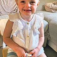 Lana a rejoint le concours — aidez-le/la à gagner de superbes lots ! child, smiling, sitting, white_top, denim_shorts, chair, indoor, home, cozy, blanket, sofa, person, happy, young, cute, girl, furniture, casual_clothing, shorts, relaxed