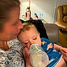 adult, baby, blurred_face, bottle, casual, child, clothing, comfort, couch, family, feeding, feeding_time, holding, home, indoor, infant, lamp, person, relaxing, sleepy