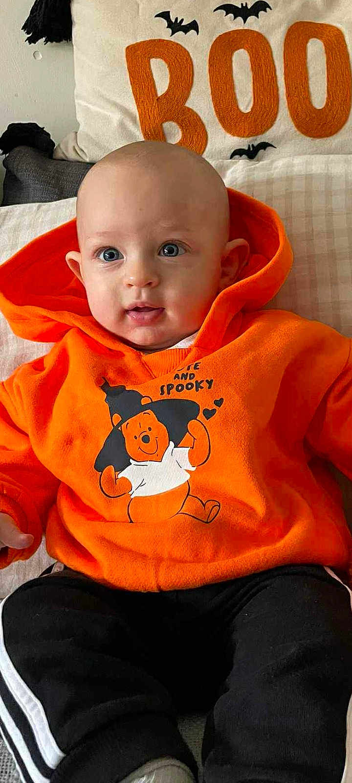 Elio participe au concours pour gagner de l'argent avec cette photo : baby, child, hoodie, orange_clothing, winnie_the_pooh, halloween, bat, cushion, pillow, text, face, eyes, sitting, black_pants, white_stripes, indoor, cute, infant, portrait, smiling