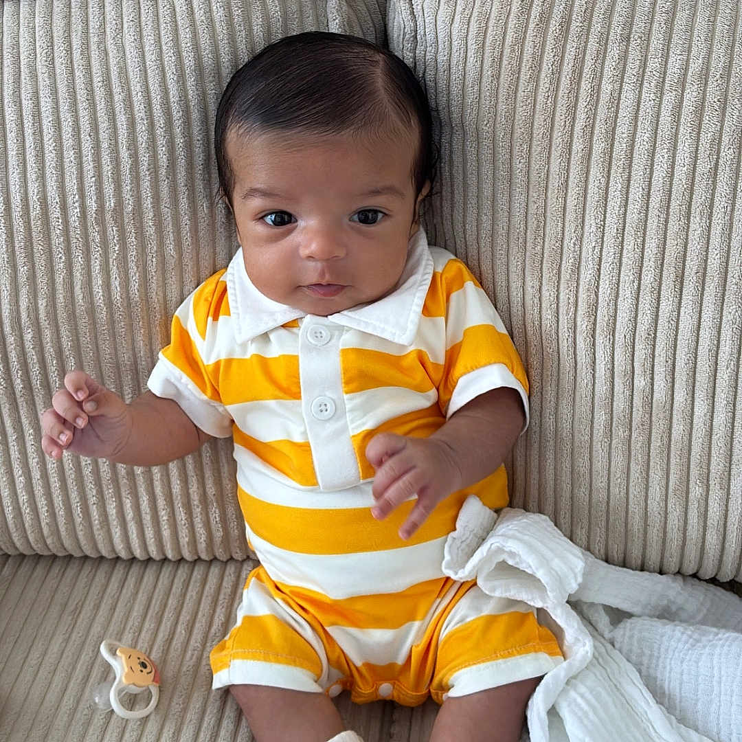 Zahir a rejoint le concours — aidez-le/la à gagner de superbes lots ! baby, child, couch, curious, cute, face, furniture, head, indoor, infant, pacifier, pillow, portrait, seated, small_hands, socks, soft_fabric, striped_clothing, white, yellow