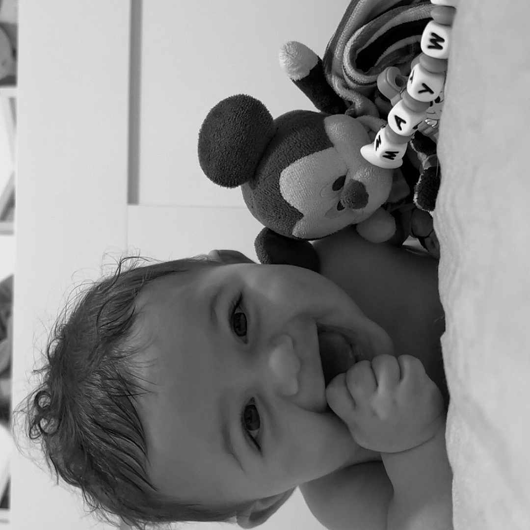 Maywen participe au concours pour gagner de l'argent avec cette photo : baby, bead_bracelet, black_and_white, child, close_up, cute, face, hand, happy, indoors, infant, lying_down, mickey_mouse, person, playful, plush_toy, portrait, smiling, soft_surface, toy