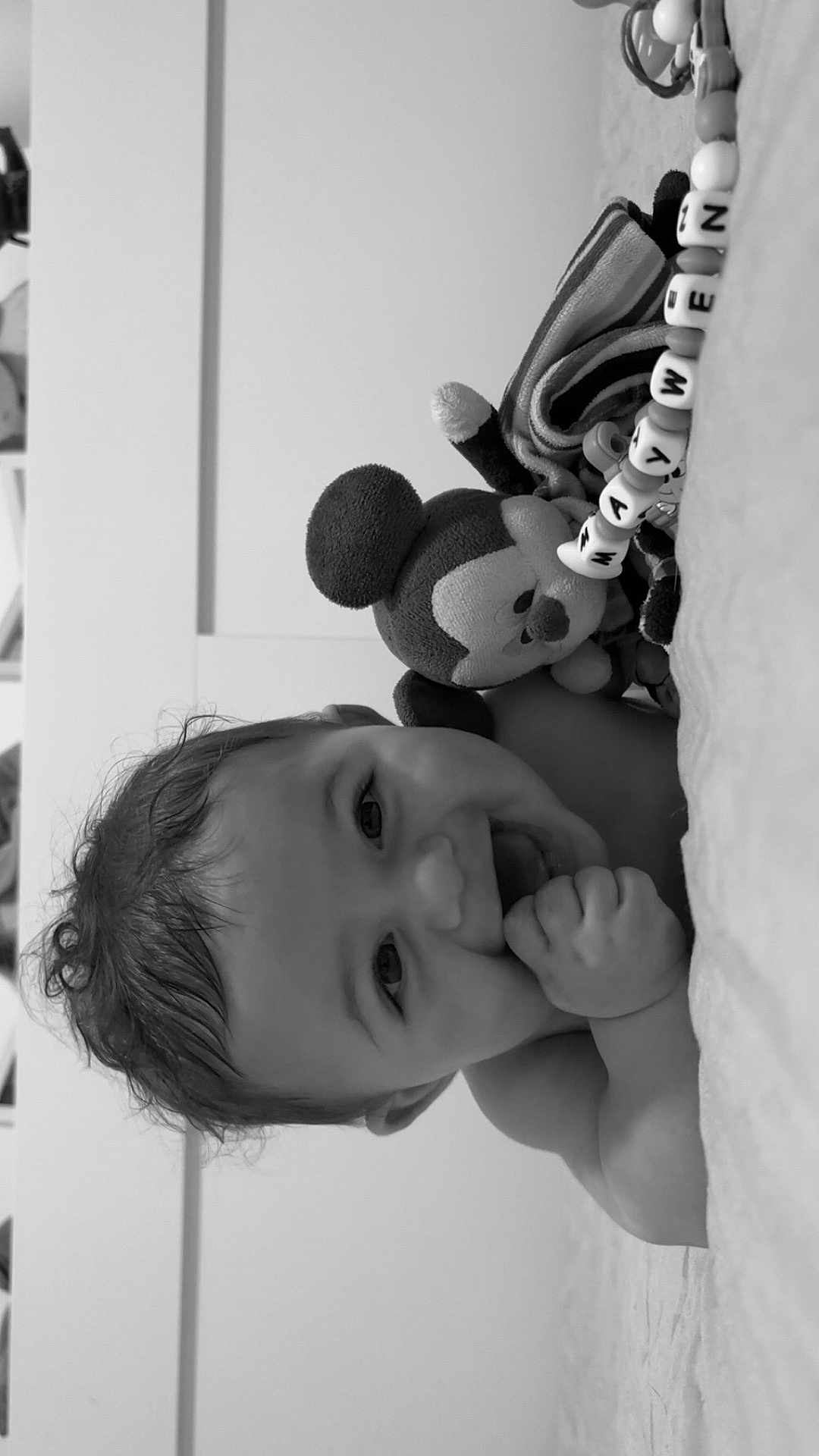 Maywen participe au concours pour gagner de l'argent avec cette photo : baby, smiling, black_and_white, plush_toy, mickey_mouse, bead_bracelet, child, happy, cute, indoors, portrait, hand, toy, face, infant, lying_down, soft_surface, close_up, person, playful