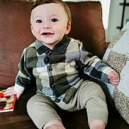 Aaron a rejoint le concours — aidez-le/la à gagner de superbes lots ! baby, child, smiling, plaid_shirt, beige_pants, barefoot, couch, indoor, happy, blue_eyes, holding_book, portrait, cute, seated, cozy, young_child, person, home, infant, comfortable