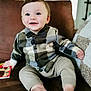 baby, child, smiling, plaid_shirt, beige_pants, barefoot, couch, indoor, happy, blue_eyes, holding_book, portrait, cute, seated, cozy, young_child, person, home, infant, comfortable
