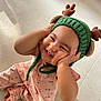 Paolina participe au concours pour gagner de l'argent avec cette photo : baby, child, smiling, green_hat, antlers, pink_pajamas, cherry_print, cute, happy, sitting, floor, indoor, infant, hands_on_face, candid, portrait, headwear, playful, young_child, expression