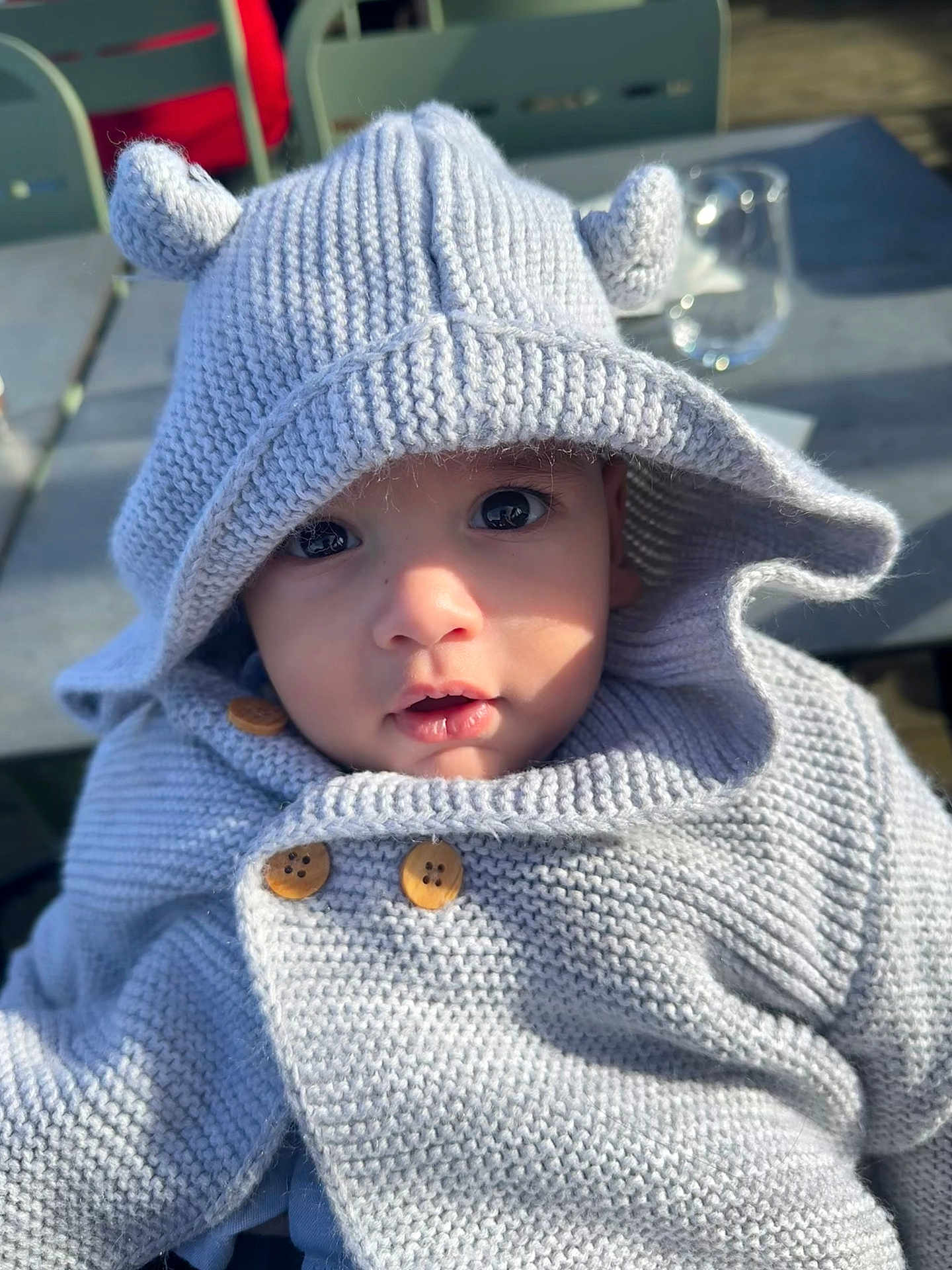 Baby Love a rejoint le concours — aidez-le/la à gagner de superbes lots ! baby, buttons, chair, child, cozy, curious, cute, ears, eyes, face, glass, hood, infant, knitted_hoodie, outdoor, portrait, sitting, sunlight, table, warm_clothing