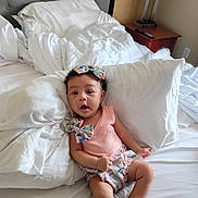 Kaliyah is registered to the contest to win money with this photo: baby, infant, child, bed, pillow, blanket, headband, clothing, cute, indoors, sleepwear, person, skin, smile, expression, furniture, room, lamp, nightstand, curious