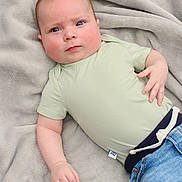 Asher is registered to the contest to win money with this photo: baby, infant, child, face, blue_eyes, green_shirt, jeans, blanket, soft_texture, lying_down, cute, chubby_cheeks, hand, casual_clothing, indoors, portrait, expression, skin, head, young