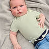 baby, infant, child, face, blue_eyes, green_shirt, jeans, blanket, soft_texture, lying_down, cute, chubby_cheeks, hand, casual_clothing, indoors, portrait, expression, skin, head, young