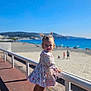 beach, child, coast, daylight, dress, footwear, girl, ocean, outdoor, pigtails, playful, railing, sand, shadows, sky, smile, summer, sunny, toddler, vacation