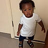 toddler, child, indoor, door, white_tshirt, navy_shorts, black_slides, floor, curious, standing, person, young_child, hair, looking_up, expression, footwear, casual_clothing, wall, floor_tiles, human